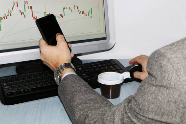 Yakın çekim-masada bir bilgisayar, bir plastik tek kullanımlık fincan kahve, bir akıllı telefon, bir hisse senedi grafiği için bir monitör var