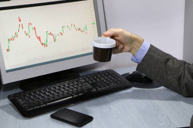 Yakın çekim-masada bir bilgisayar, bir plastik tek kullanımlık fincan kahve, bir akıllı telefon, bir hisse senedi grafiği için bir monitör var