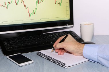 Yatırımcı grafikler görünüyor ve defterindeki çiziminden kalemle notlar alır. Sonraki bir smartphone olduğunu