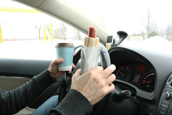 the driver at the wheel drinks coffee, eats the hot dock and talks on the phone