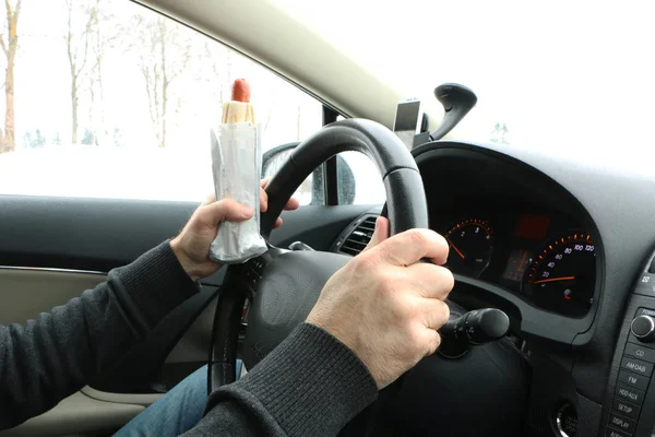 the driver at the wheel drinks coffee, eats the hot dock and talks on the phone