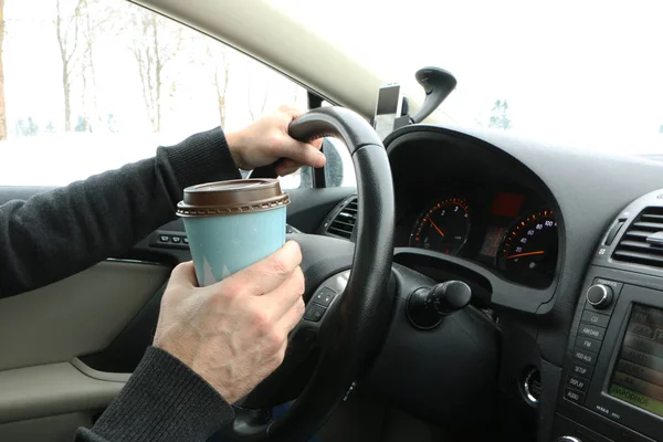 the driver at the wheel drinks coffee, eats the hot dock and talks on the phone