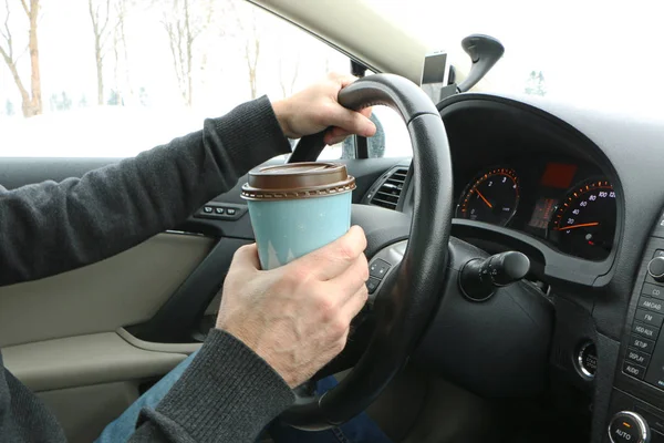 the driver at the wheel drinks coffee, eats the hot dock and talks on the phone