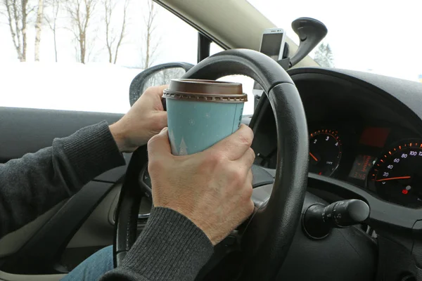 the driver at the wheel drinks coffee, eats the hot dock and talks on the phone