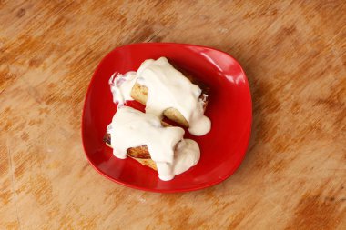 Kırmızı plaka üzerinde ekşi krema soslu kızarmış krep. Arka plan ağaç ve beyaz. Gıda, Rus mutfak.