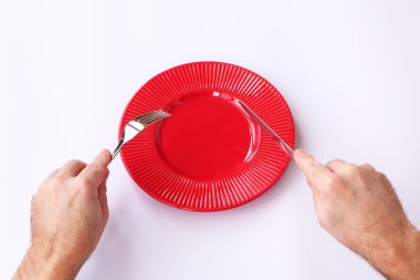 Yakın çekim-kırmızı plaka beyaz bir arka plan üzerinde. Onun el bir bıçak ve çatal.