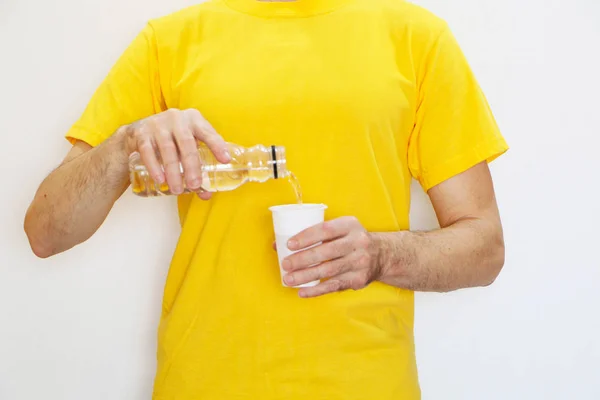 Primer plano: un hombre vierte agua de una botella de plástico en un plasti —  Fotos de Stock