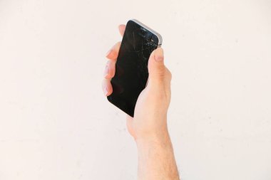 Kırık bir akıllı telefon ekranı beyaz arka planda, genç bir adamın elinde..