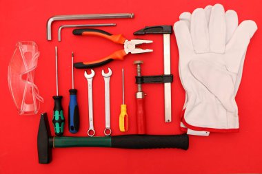 Kırmızı arka planda yeni el aletleri, maske, gözlük ve eldivenler. Kırmızı arka planda güvenli bir iş için yeni el aletleri ve koruyucu ekipmanlar..
