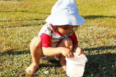Küçük bir çocuk oyun alanında oynuyor. Küçük kız plastikle kayıyor. Küçük kız yazın kumsalda oynar.
