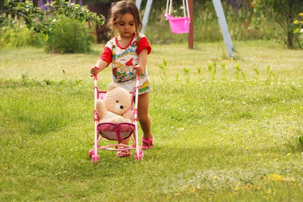A child plays in the summer on the playground. A little girl plays with a baby carriage. The child sunbathes in the summer on the nature.
