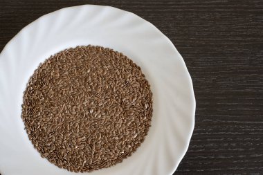 Kahverengi bir masada yemek pişirmek için tabakta kurutulmuş keten tohumu. Beyaz tabakta keten tohumu