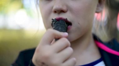 Bir waffle koni içinde dondurma siyah yeme Bebek kız, yeşil yaprakları ile ağaçların arka planda yaz aylarında elinde dondurma ile bebek kız o bir gün yiyor 