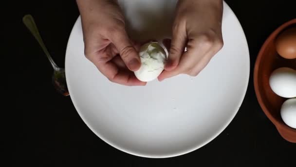 家庭で鶏の卵の卵の殻から手は白と黒いテーブルの上の白い皿に茶色のさまざまな色の卵から卵殻を削除します — ストック動画