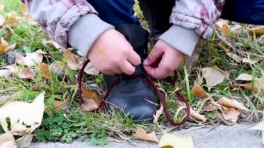  Sarı yapraklar ve yeşil çim bir arka plan üzerinde siyah deri çizmeler için kırmızı bağcıklar bağlayan bir çocuk. Bağcıkları çözdüğünde. 
