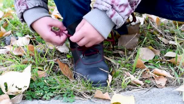一个在黄叶和绿草的背景上系上黑色皮靴的红色花边的孩子 当你走的花边解开 — 图库视频影像