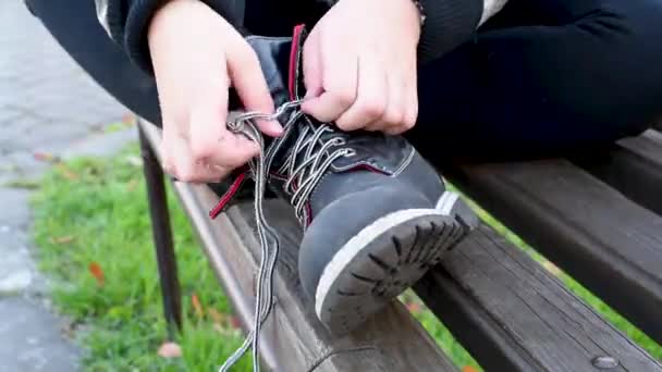 孩子们把鞋带绑在黑色皮靴上 坐在公园的街道长凳上 — 图库视频影像