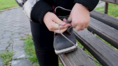 Siyah deri çizme ayakkabı bağcığı bağlama, parkta sokak bir bankta oturmuş çocuk . 