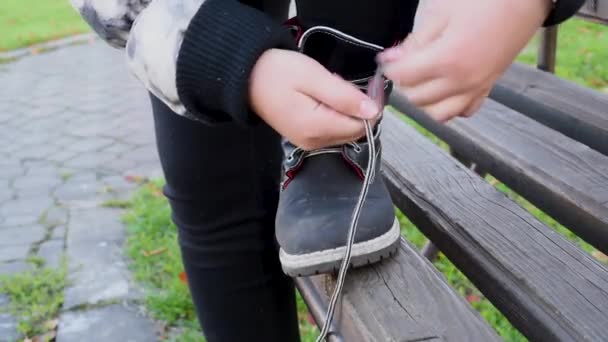 Ребенок Завязывает Шнурки Черных Кожаных Сапогах Сидит Уличной Скамейке Парке — стоковое видео