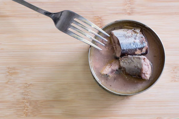 Bir açık demir kavanozu kendi suyu konserve balık ahşap bir masa üzerinde duruyor. Lezzetli balık, yemeye hazır. 