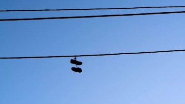 Spor ayakkabıları elektrik kablolarını yakaladı ve rüzgarda sallanan mavi gökyüzüne karşı yere yüksek asılı 