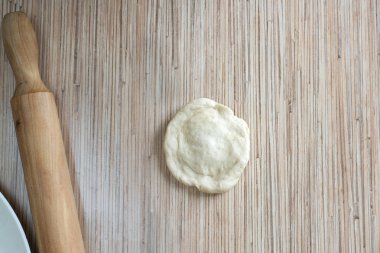 Mutfak masasındaki hamur hamuru merdaneyle rulo haline getirilir. Doldurulmuş bir turta yapmak için. Masanın yüzeyinde hamur pastası var.