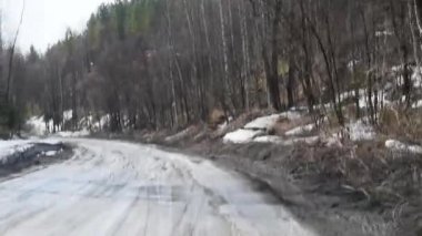Erken ilkbaharda ağaçlar çalılar arasında kırsal delikler ve su birikintileri ile Kir yol , yol kenarlarında kar eriyen gün ışığında erken ilkbaharda kaba bir ülke yolda sürüş 