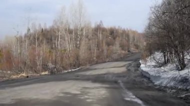 Erken ilkbaharda ağaçlar çalılar arasında kırsal delikler ve su birikintileri ile Kir yol , yol kenarlarında kar eriyen gün ışığında erken ilkbaharda kaba bir ülke yolda sürüş 