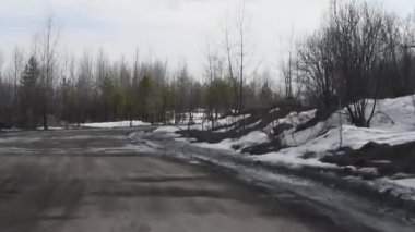 Erken ilkbaharda ağaçlar çalılar arasında kırsal delikler ve su birikintileri ile Kir yol , yol kenarlarında kar eriyen gün ışığında erken ilkbaharda kaba bir ülke yolda sürüş 