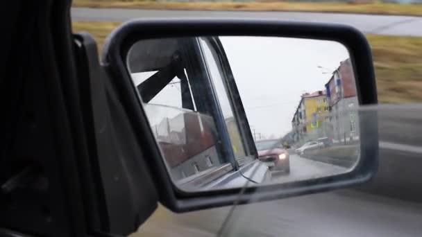 透过复古汽车的脏镜 一条房子的道路和一辆开着小灯的车在后面行驶 右侧脏车后视镜 后视镜 — 图库视频影像