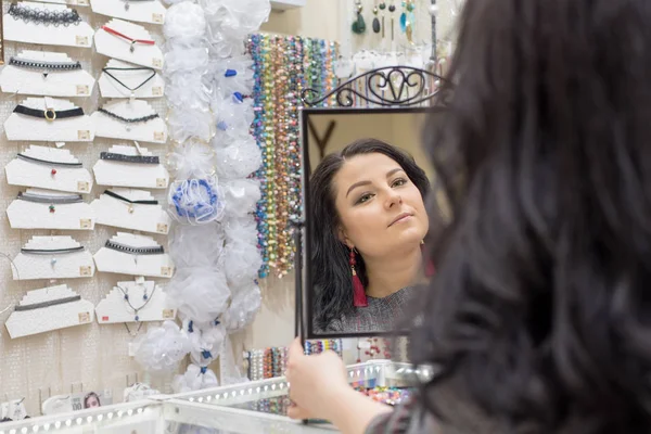 Yeşil gözlü güzel bir kız yeşil gözlü takı ve takı Esmer bir butik aksesuar küpe ve bilezik alarak aynaya bakar aynada kendini hayran