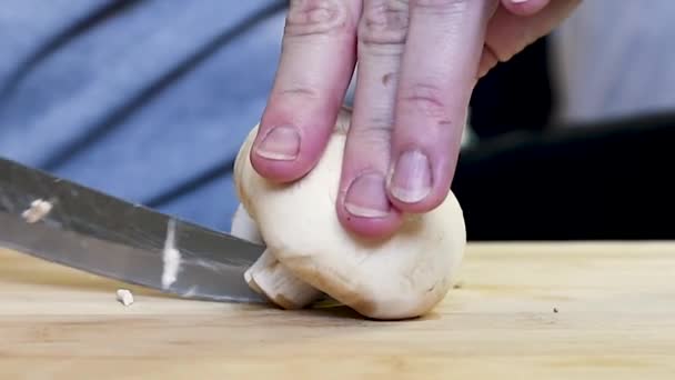 女性は台所で自宅で黒いハンドルを持つナイフで木製のボードにキノコをカットします 調理用の木製ボード上のキノコ切断キノコのクローズアップ — ストック動画