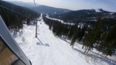 Kabinden camdan çekim, dağ ve kayak pistleri manzarası. Kaldırma ve alçaltma kabinleri, kayak merkezinde hareket halindeki asansörün çeşitli mekanizmalarının gerilmiş kablolar üzerinde yukarı ve aşağı hareket ettirilir 