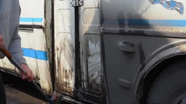 Yolculuktan sonra otobüsü özel bir fırça ve suyla yıkamak. Bir adam açık havada kirli bir otobüsü yıkıyor.