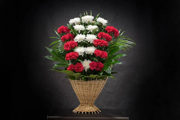 The flower arrangement of the flowers in the basket is used for funerals and bookmarks. Mourning card with a place for inscription. Ritual funeral basket with flowers on a black background