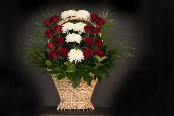 The flower arrangement of the flowers in the basket is used for funerals and bookmarks. Mourning card with a place for inscription. Ritual funeral basket with flowers on a black background