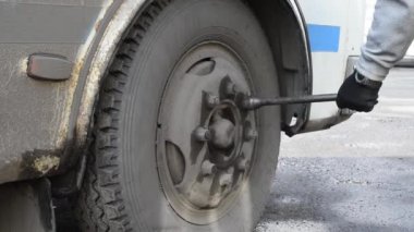 Adam eski bir otobüsün yakın çekim tekerlekleri üzerinde fındık sıkılaştırır. Doğal ışıkta açık havada önlemek ve test etmek için tekerlek üzerindeki somunları sıkın