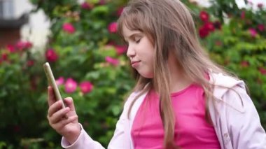 Kız çiçek açan gül bir arka plan bahçede telefonda bir selfie alır. Sarışın saçlı Avrupalı kız akıllı telefonunda kendi fotoğraflarını çekiyor
