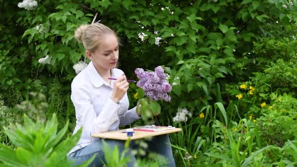若い女の子 創造性に従事するアーティストは 庭でライブライラックを描きます 庭のライラックを背景にした少女芸術家 — ストック動画