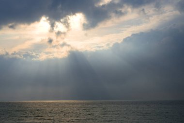 Bulutların arasından gelen güneş ışınlarındaki deniz. Bulutlu bir günde güneş ışığı ışınlarında deniz yüzeyi