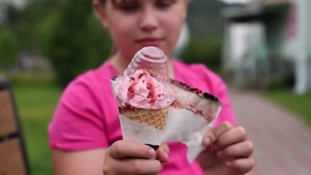 ガーリーはアイスクリームを食べたい 女の子はイチゴアイスクリームからラッパーを削除します — ストック動画