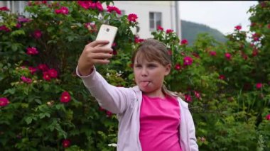 Sarışın saçlı Avrupalı bir kız akıllı telefonunda kendi fotoğraflarını çekiyor. Kız çiçek açan gül bir arka plan bahçede telefonda bir selfie alır