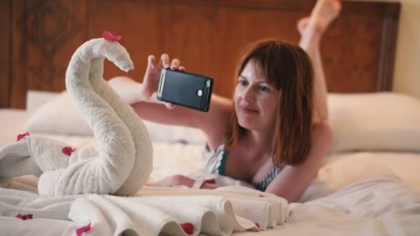 少女は電話でタオルで作られた白鳥の写真を撮る — ストック動画
