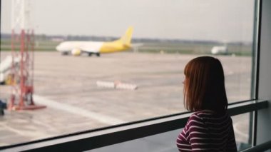 Havaalanı. Kız pencereden uçağa bakıyor.