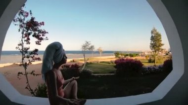 Denize bakan pencere. Bir kız bir kütüğe oturur ve bir cep telefonuna bakar..