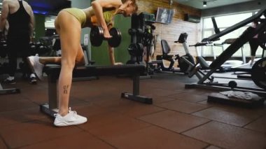 Spor salonu. Kız spor salonunda bir dambıl ile kasları sallar