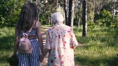 Büyükanne ve torunu el ele tutuşup parkta yürüyorlar.