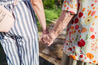 Büyükanne ve torunu el ele tutuşup parkta yürüyorlar.