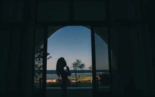 Window overlooking the sea. A girl sits in a lotus position on a