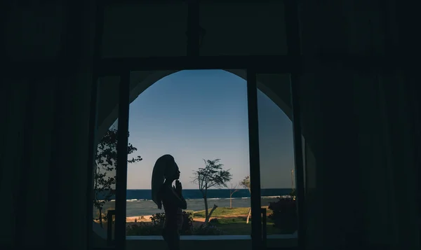 Raam met uitzicht op de zee. Een meisje zit in een lotuspositie op een — Stockfoto